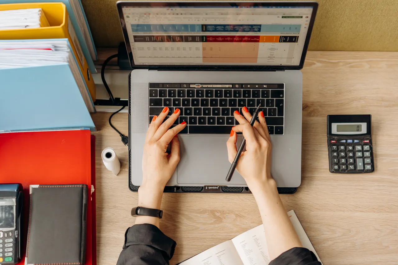 Hands typing on a laptop beside folders and a calculator